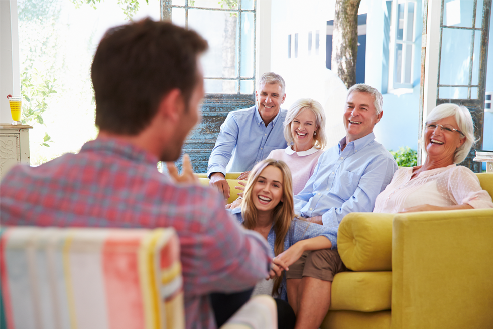 Image of family laughing together, sitting down on sofa and chair